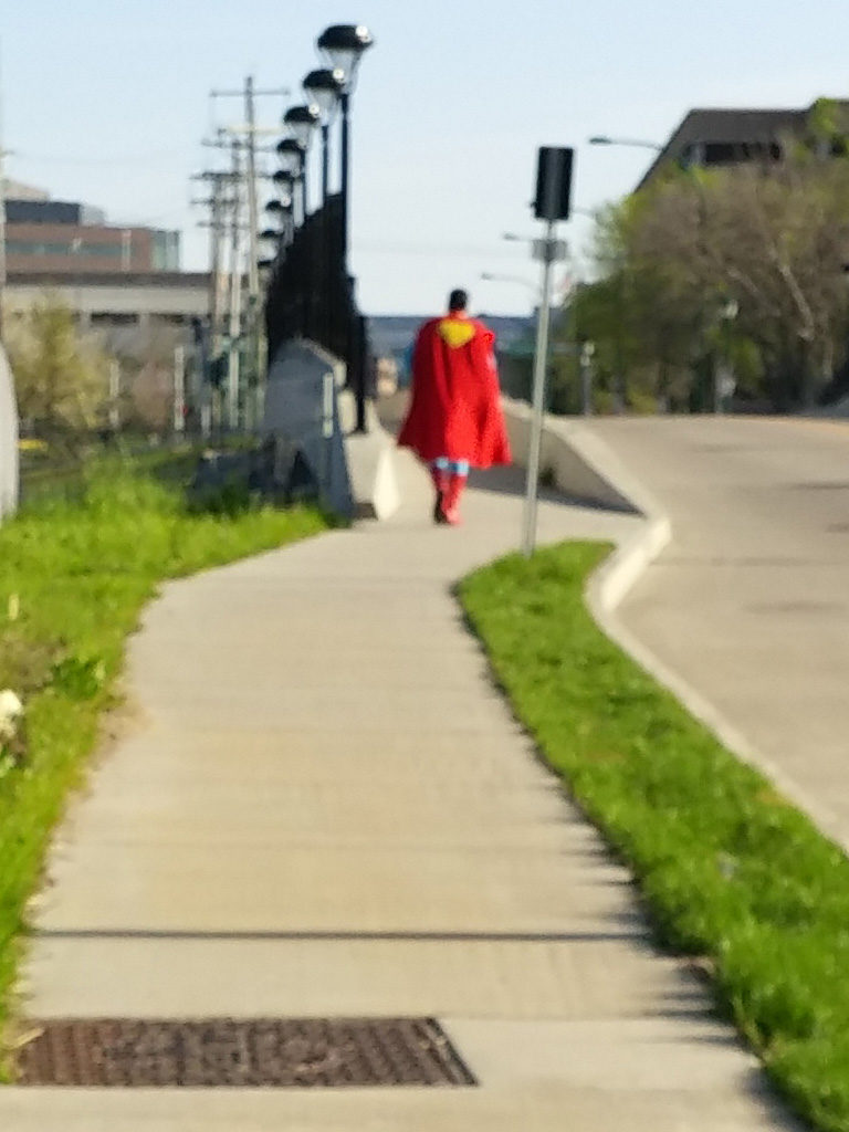 blurry photo of man in Superman costume walking away down a sidewalk