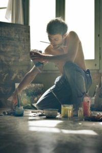 photo of a shirtless man kneeling on the floor and painting