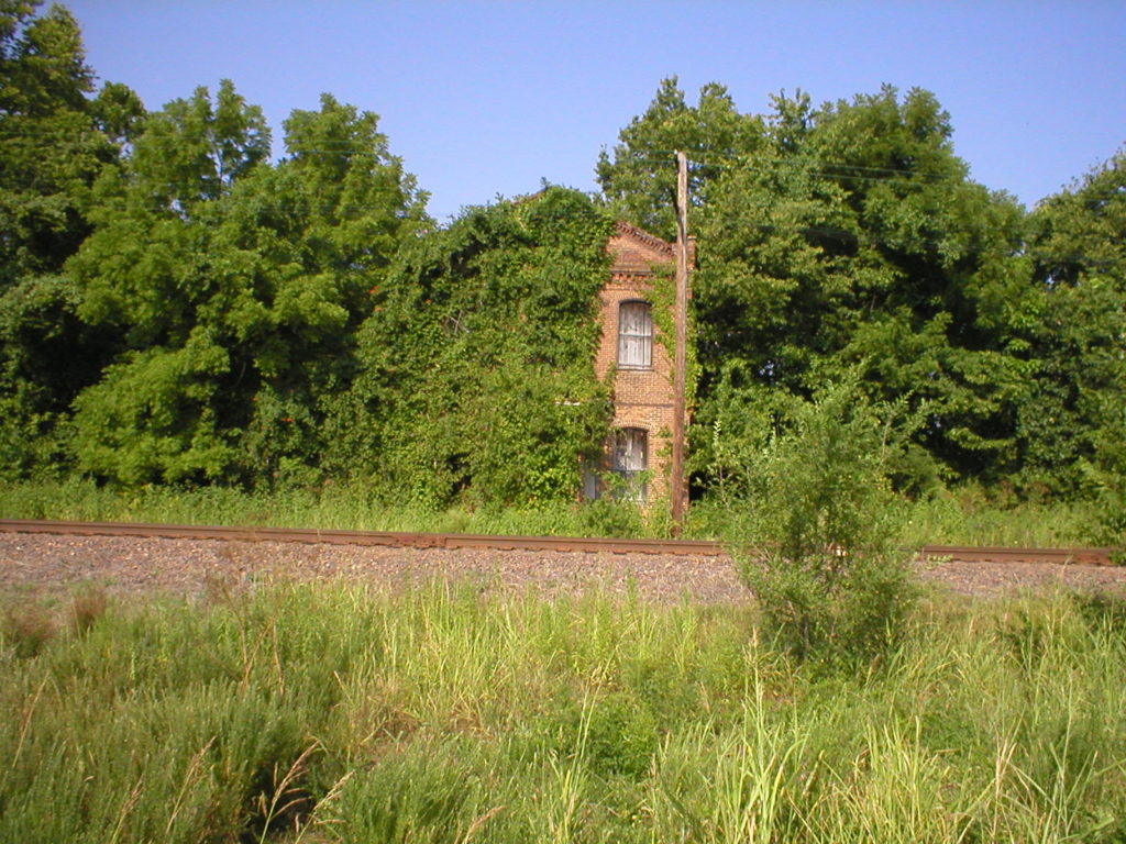 photo of a partially collapsed old hotel building near railroad tracks