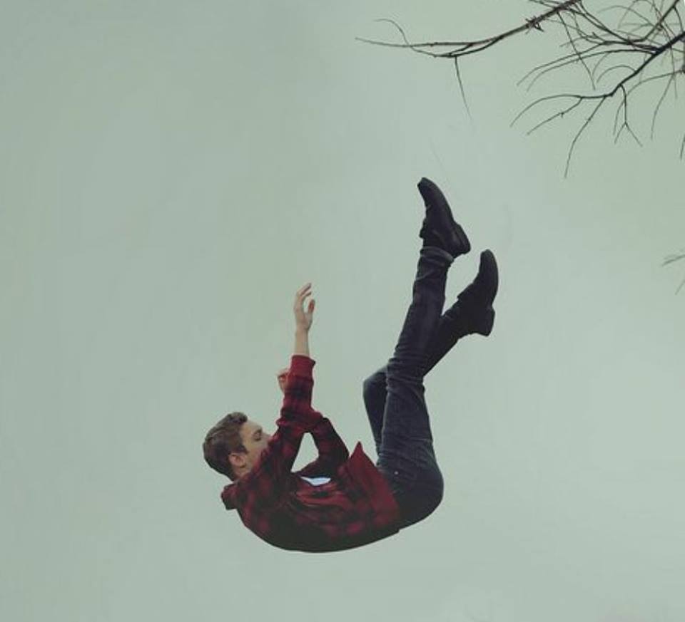 Photo of a boy falling through the air with a tree branch in the upper righthand corner.