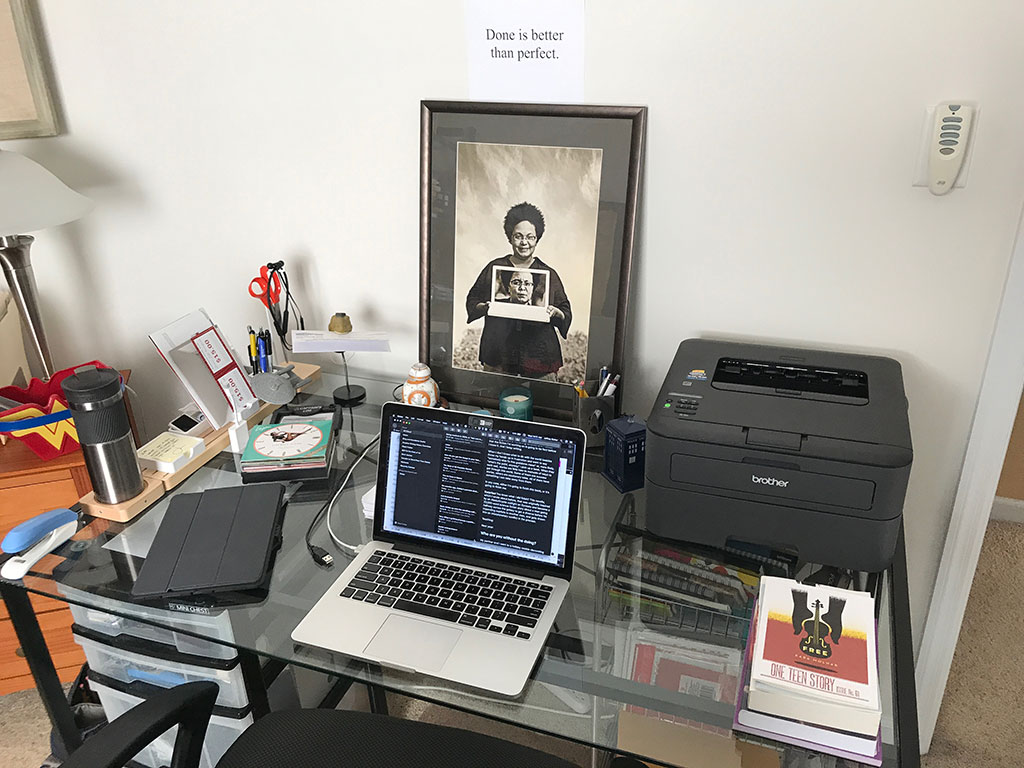 A photo of my desk with the words "Done is better than perfect" printed and taped to the wall above it.