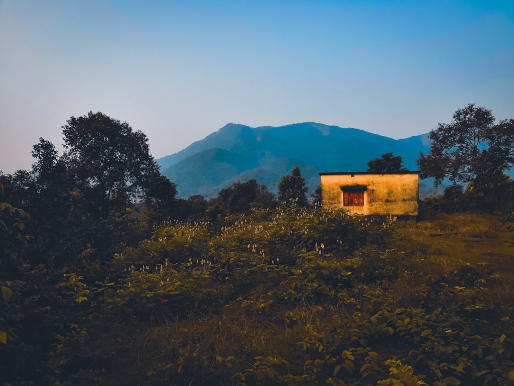 Photo of a small cabin in a grassy area with mountains in the background