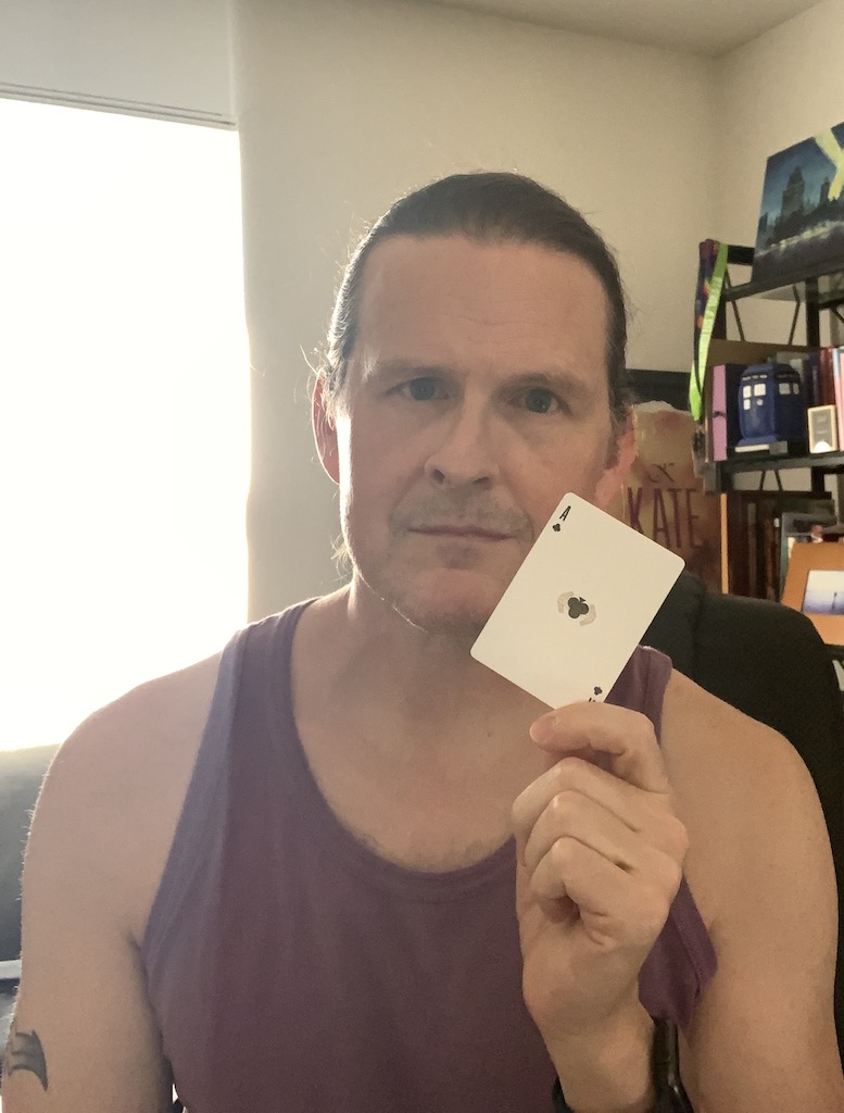 Photo of white male (me) holding a playing card, specifically the ace of clubs.