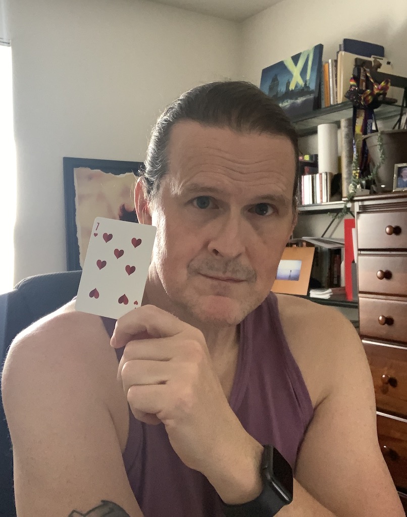 A white male (me) holding a playing card, specifically the seven of hearts.